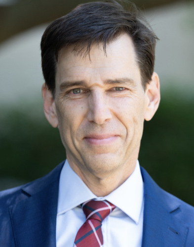 A man in a blue suit and red striped tie smiles at the camera.